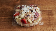 Fruit salad with granola and  cream in a clear plastic container on a wooden surface