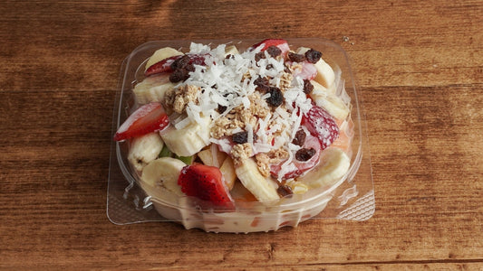 Fruit salad with granola and  cream in a clear plastic container on a wooden surface