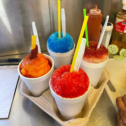 Four vibrant raspas in foam cups topped with tamarindo, chamoy, and flavored syrup, served fresh by Frosty Brothers.