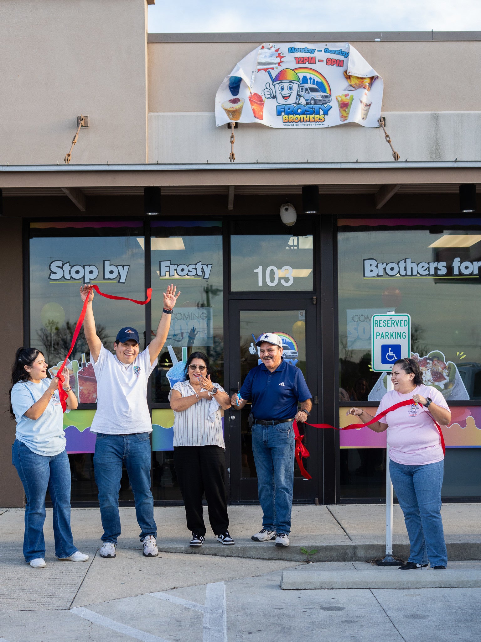 Frosty Family cutting a ribbon in front of the store with a colorful sign above the entrance.